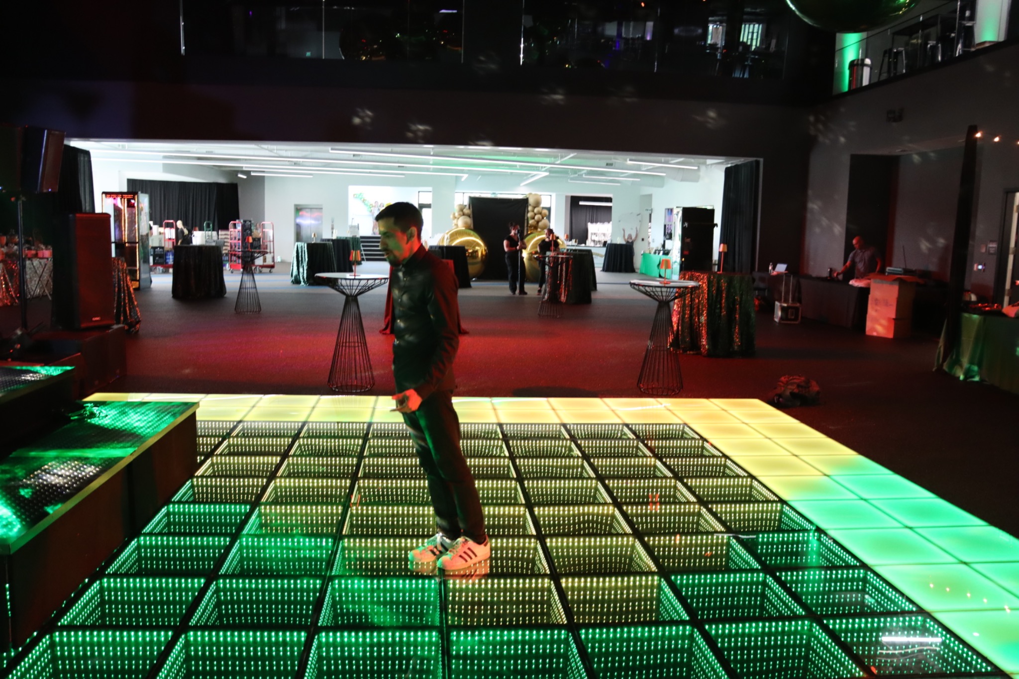 An illuminated green and gold dance floor with a performer and event setup in the background
